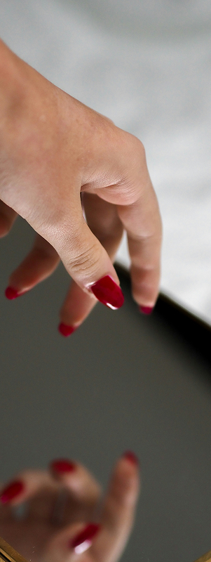 A hand with red fingernails hovering above a mirror