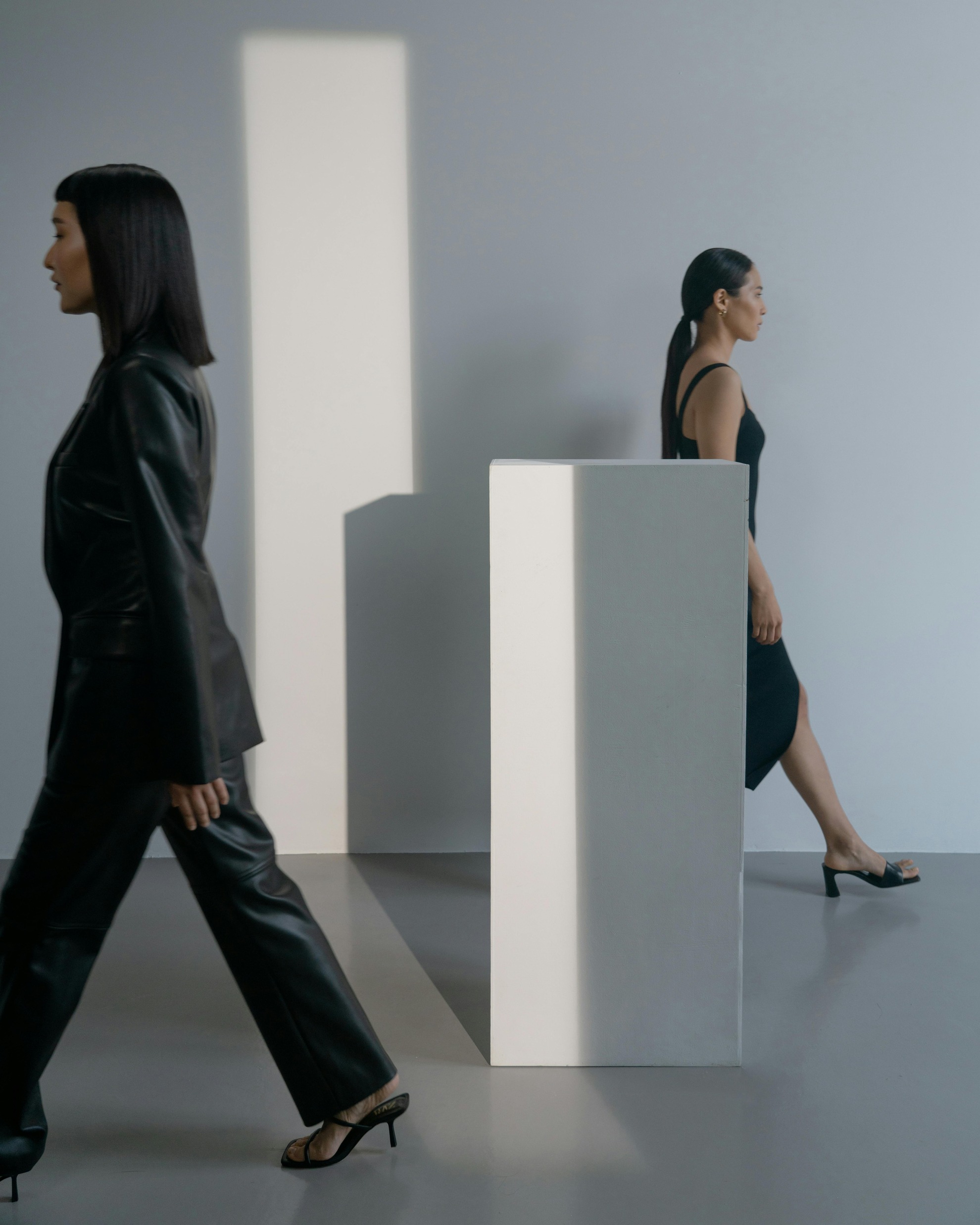 Models in black walking in opposite directions in a white room